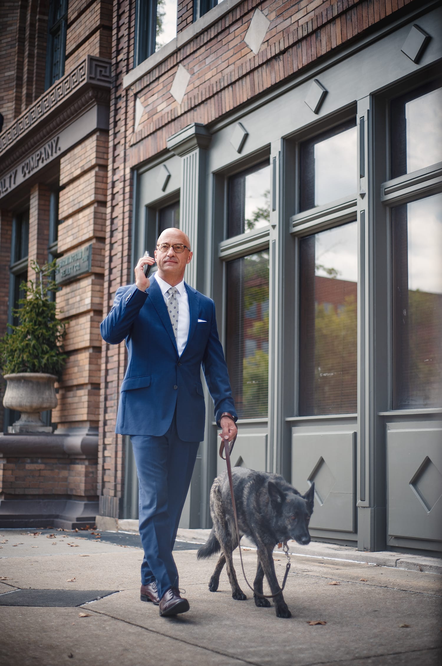 Lawyer on a phone walking a dog on a sidewalk in front of a building